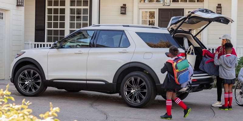 White SUV parked in a driveway with people loading items into the rear cargo area.